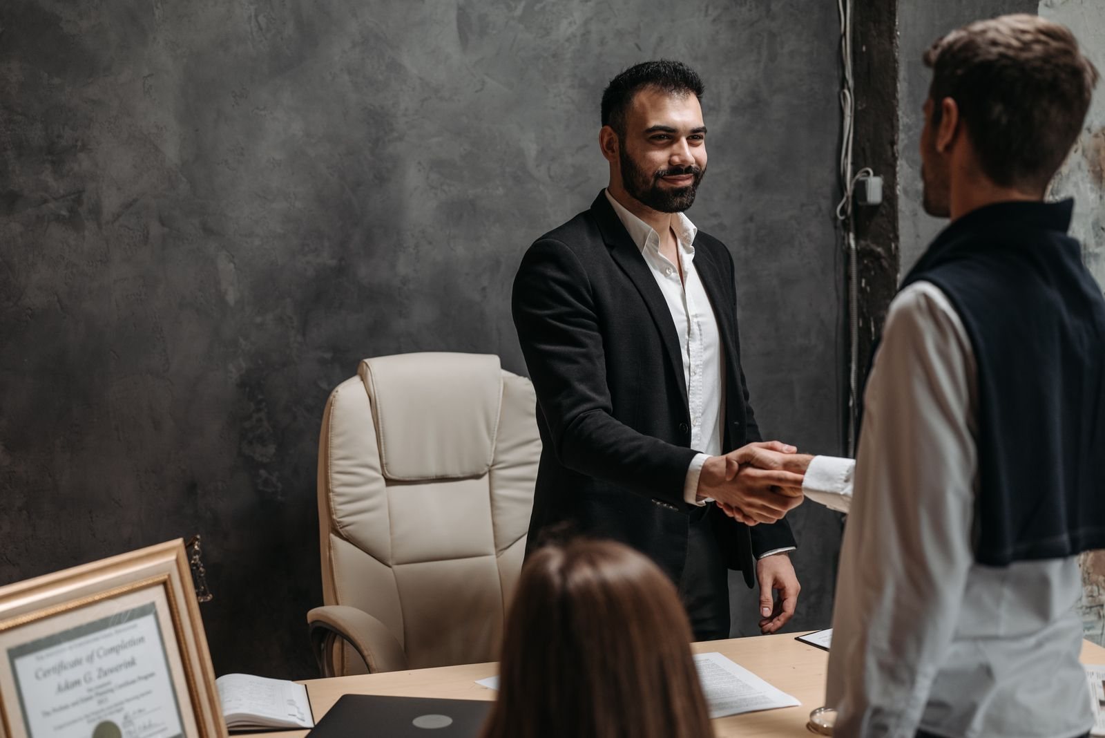 Two professionals shaking hands across an office desk