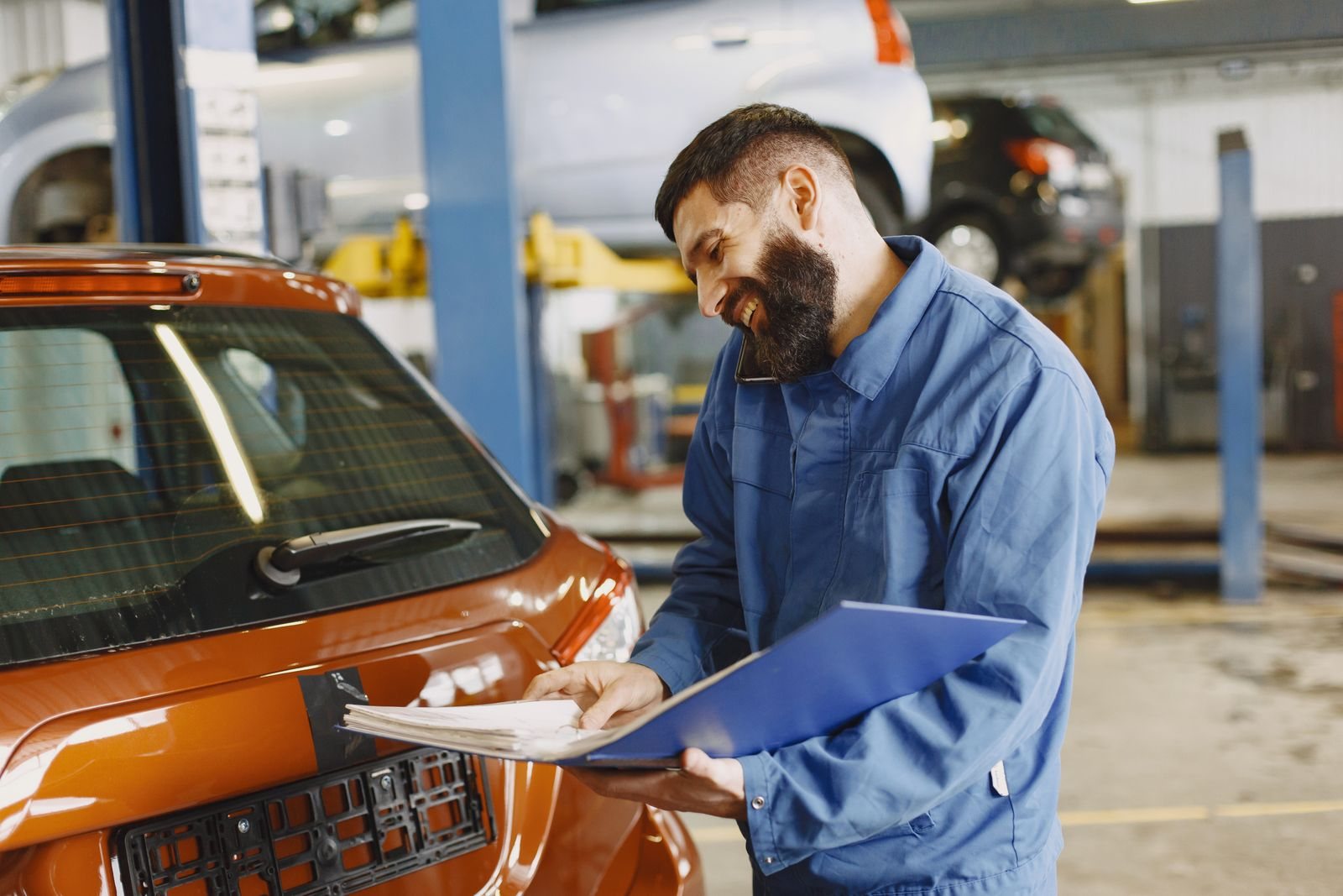 An auto mechanic reviewing a repair order beside a customer's car