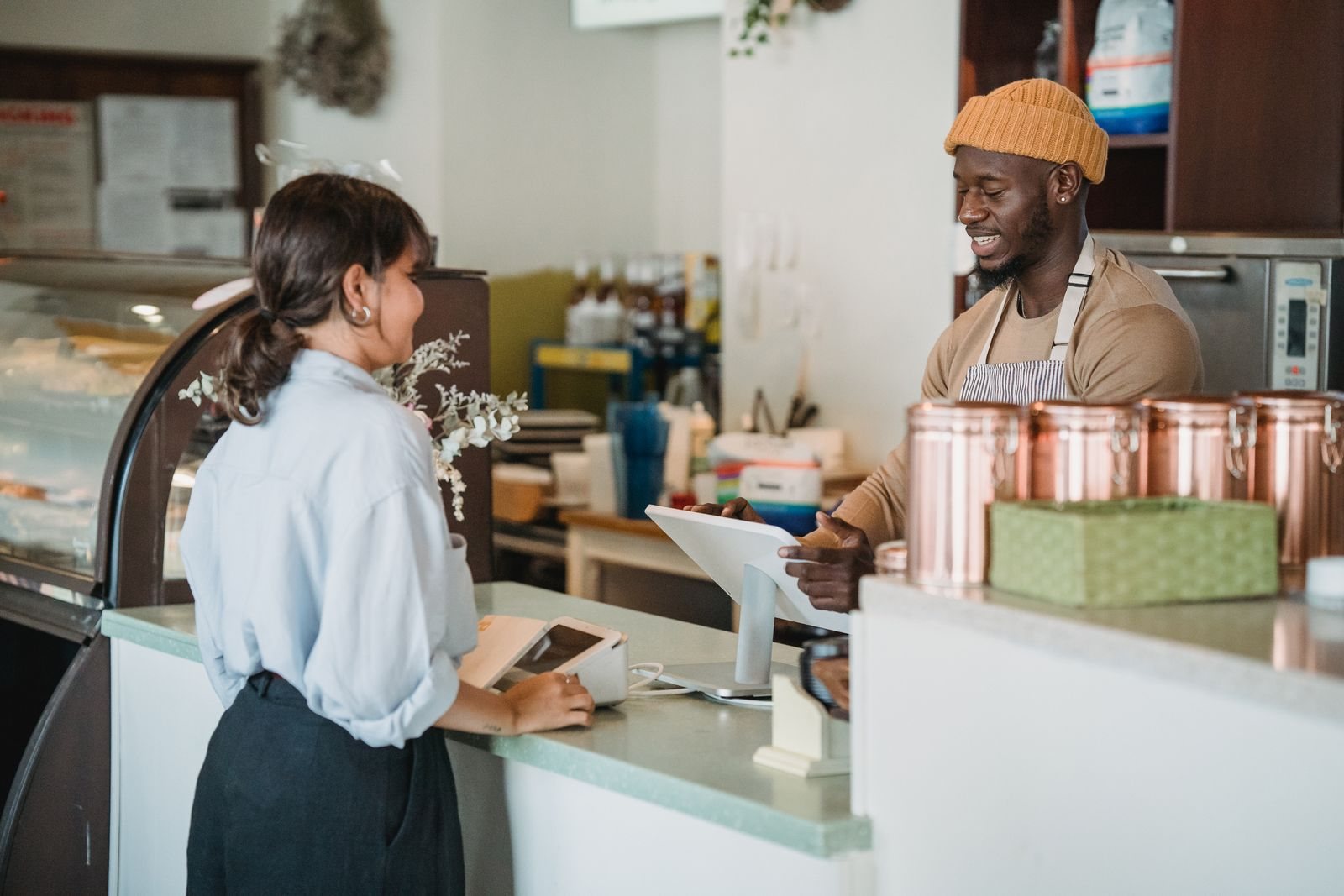 A bakery owner serving a customer and managing an order at the counter