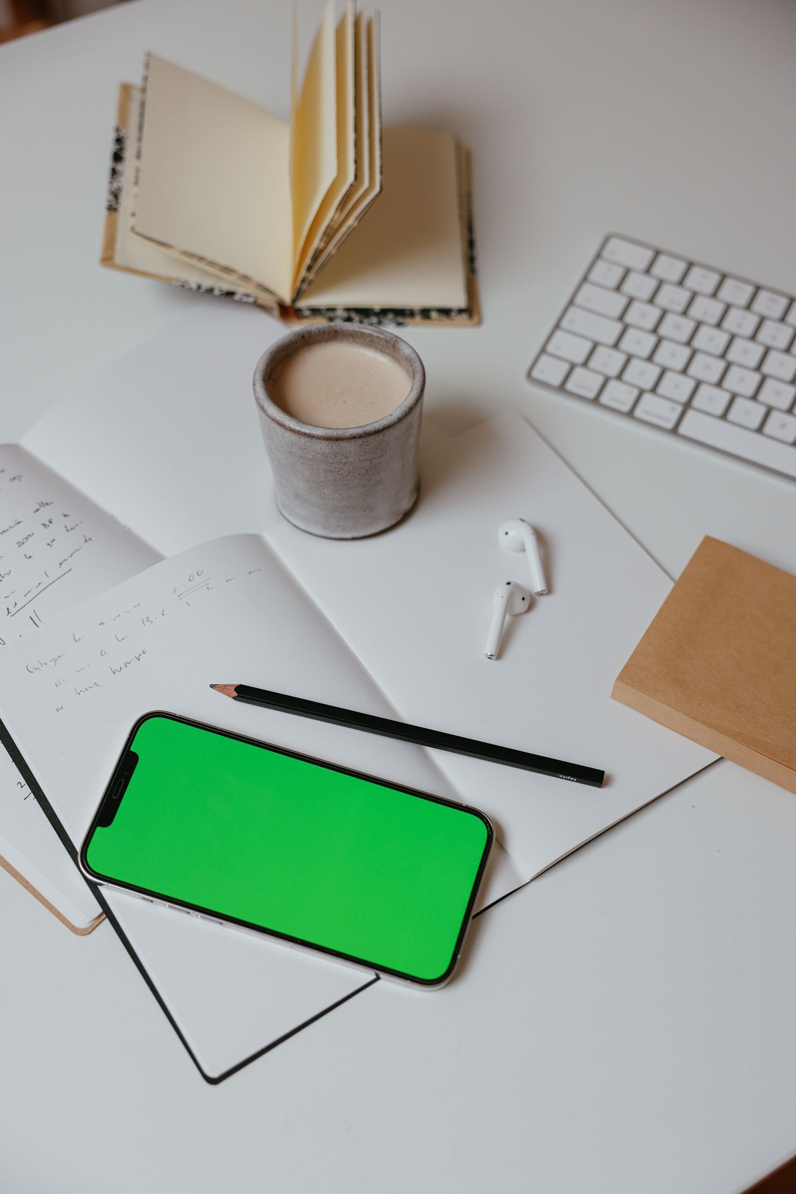 A smartphone beside a keyboard, coffee, and notebooks on a desk